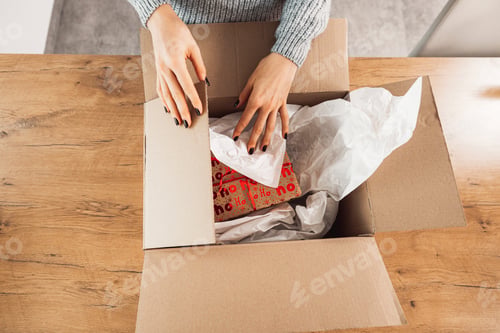 Preview: Unrecognizable woman, top down view packaging a Christmas present in a larger box, to send with mail