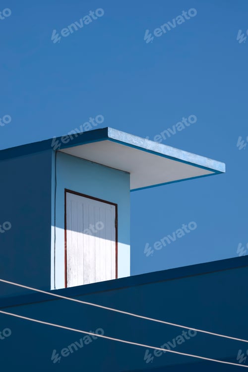 Preview: Sunlight and shadow on surface of white wooden rooftop door of blue house building against blue sky