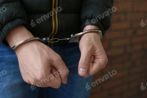 Preview: Criminal detained in handcuffs against wall, closeup