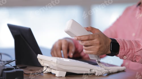 Preview: Holding handset of the telephone and working in laptop
