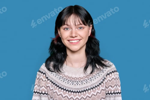 Preview: Portrait of young woman looking at camera in winter sweater on blue color studio background
