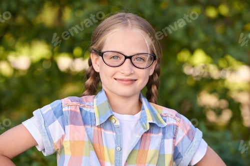 Preview: Smiling caucasian young girl with glasses in plaid shirt posing outdoors
