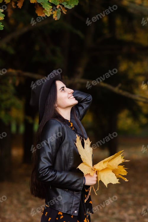 Preview: A girl in a black hat holds yellow autumn leaves in her hands