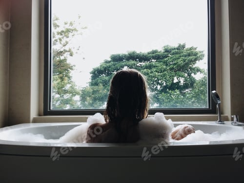 Preview: Woman relaxing in the bubble bath next to the big window