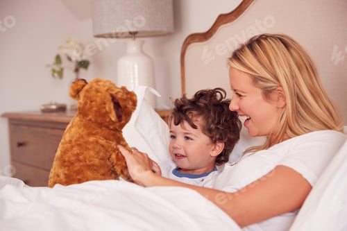 Preview: Mother And Young Son Wearing Pyjamas In Bedroom Together Playing With Cuddly Teddy Bear Toy