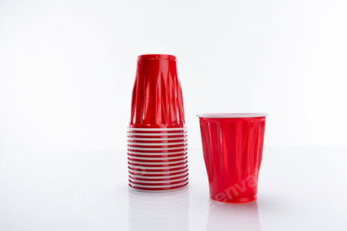 Preview: Red disposable plastic cup put next to a horizontal stack of cups against a white background