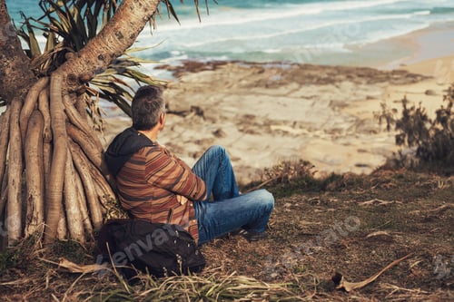 Preview: Middle-aged man sitting under the tree at the ocean