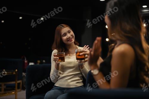 Preview: Two happy beautiful women enjoying drinks together in a cozy, dimly lit bar.