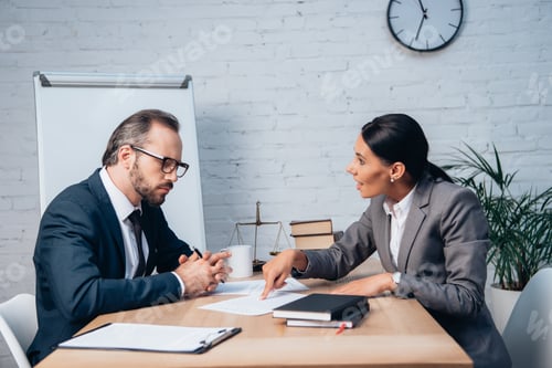 Preview: businesswoman pointing with finger at document and talking with coworker in glasses