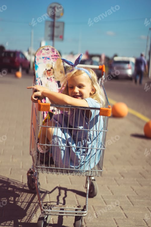 Preview: little adorable smiling kid sitting in shopping cart with skateboard