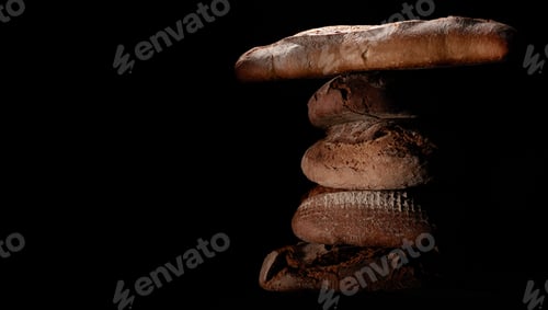 Preview: Freshly baked bread loaves and baguettes stacked on top of each other on a black background