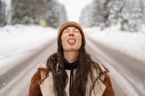 Preview: Joyful asian girl standing on forest snowy road with eyes closed and tongue sticking out