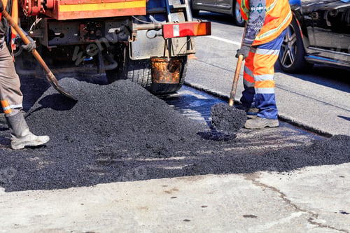 Preview: Road service worker shoveling new asphalt during construction and patching of a road