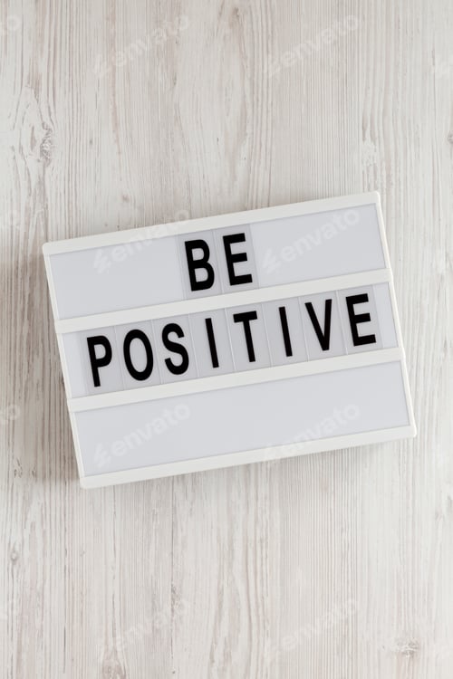 Preview: 'Be positive' words on a lightbox on a white wooden background, top view. Overhead, from above