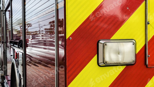 Preview: Fire truck from behind in red with yellow stripes and reflections of parking lot.
