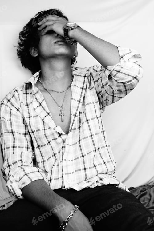 Preview: Vertical grayscale shot of a handsome South Asian man sitting with his hand on his face