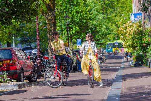 Preview: Young happy caucasian couple on bikes in old streets in Amsterdam