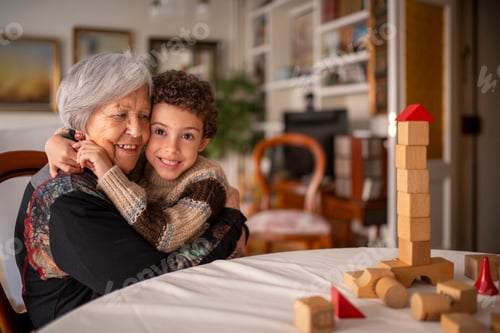 Preview: Grandson hugging grandmother at home while playing with building blocks