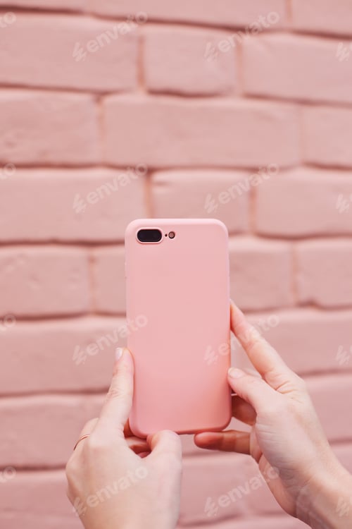 Preview: Woman holding pink mobile phone on a pink brick wall background