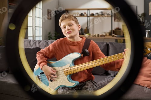 Preview: Portrait of Caucasian Boy Playing Electric Bass Guitar Sitting on Sofa