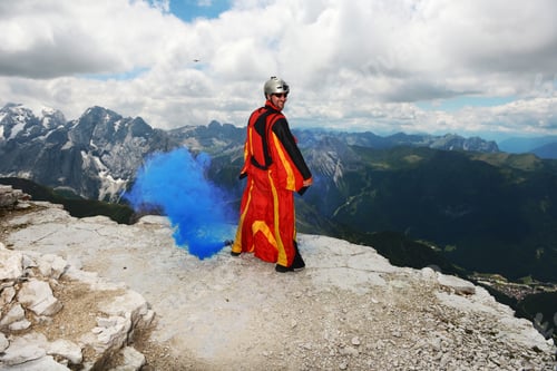 Preview: Base jumper on Dolomite mountains wearing wingsuit emitting blue smoke, Canazei, Trentino Alto Adige