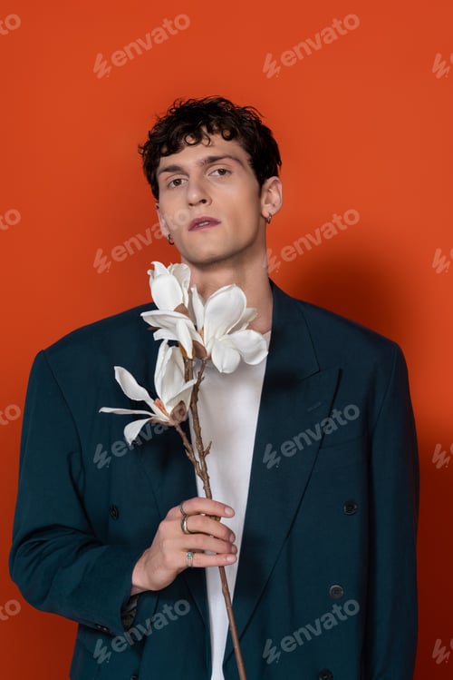 Preview: Stylish man in blue jacket holding magnolia branch on red background