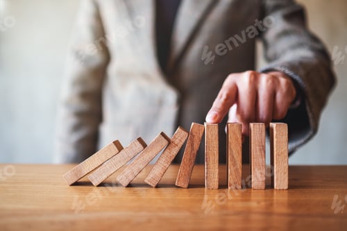 Preview: a businesswoman's finger try to stopping falling wooden dominoes blocks