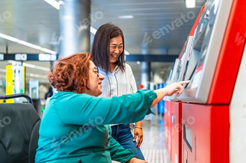 Preview: Disabled woman and smiling friend buying ticket for public transport at the station