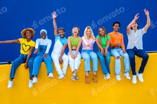 Preview: Multi-ethnic happy young people sitting on colorful retaining wall