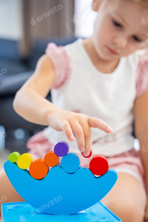 Preview: Little girl playing with wooden balancing toy on the floor in home living room. Focus on balancer