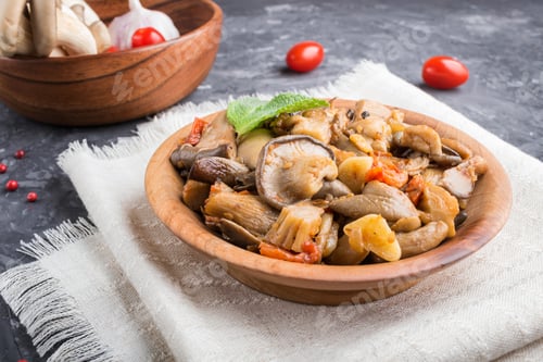 Preview: Fried oyster mushrooms with tomatoes in wooden plate on black concrete background. side view.