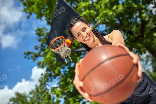 Preview: Beautiful, sporty latin girl with a basketball under the ring on a street basketball court. Sport
