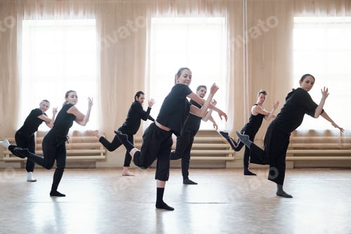 Preview: Seven young active men and women in black sportswear training in studio