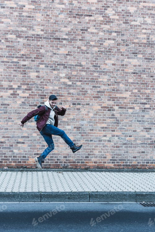 Preview: Young man jumping in front of brick wall