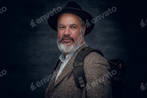 Preview: Senior man with hat and backpack against dark background