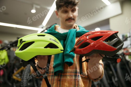 Preview: Thoughtful man choosing between two safety helmet for speed bicycle riding