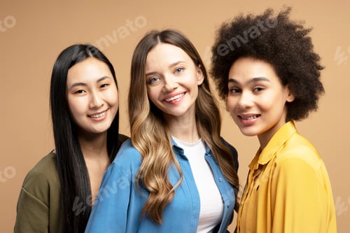 Preview: Group of young women of different ethnicities smiling together on beige background