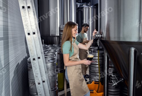 Preview: Female brewer working in craft brewery examining quality of the beer.