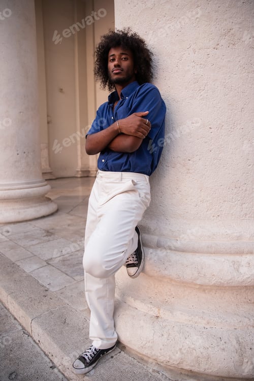 Preview: Young black boy leaning against a column in downtown looks thoughtfully ahead