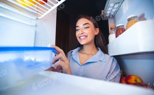 Preview: Cheerful girl taking food container with lunch from fridge