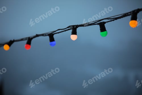 Preview: Low angle shot of colorful Christmas lights hanging on a cable on a white sky background