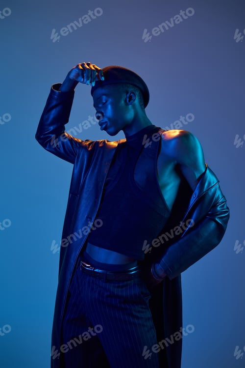 Preview: Vibrant young man showcases stylish fashion with an artistic flair in a striking blue backdrop