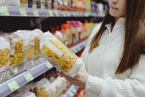 Preview: Young woman holds pasta package, shopping in grocery store.