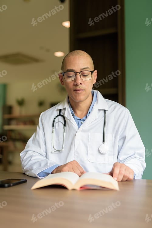 Preview: Doctor Sitting Indoors in Clinic or Hospital Area Library with Stethoscope Reading Book