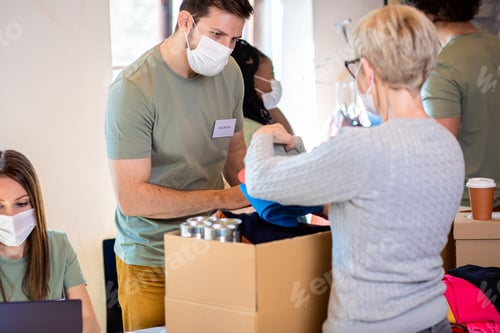 Preview: Group of volunteers with face mask working in community charity donation center.
