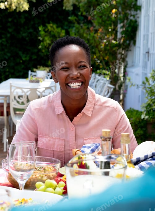 Preview: Smiling woman enjoying outdoor meal with family, surrounded by fresh fruits