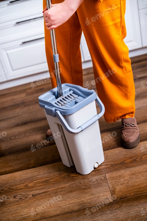 Preview: Woman cleans house with flat mop and spin bucket. Housewife in orange pants washes wooden floor
