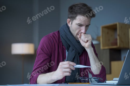 Preview: Unhealthy looking male entrepreneur in scarf around his neck coughing looks at digital thermometer