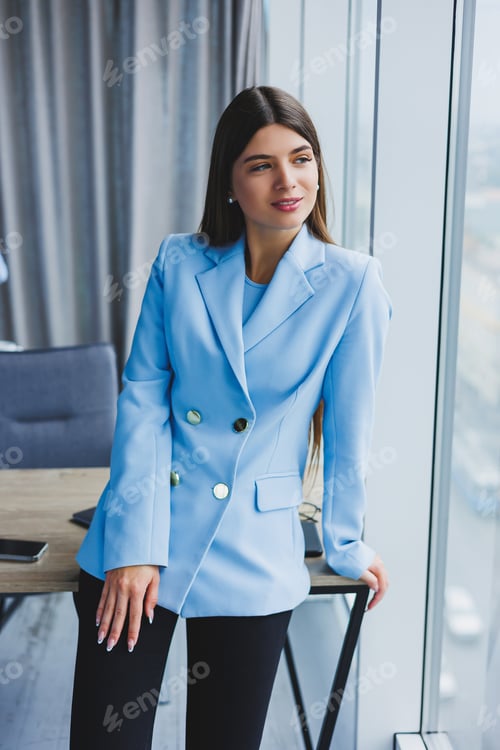 Preview: Portrait of a pretty brunette in a blue jacket in the office near the panoramic window