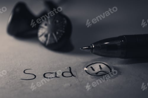 Preview: Grayscale depressing shot of a paper with the word sad and a drawn sad face under a teardrop